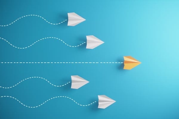 A yellow paper airplane wins the race over a group of plain white paper airplanes